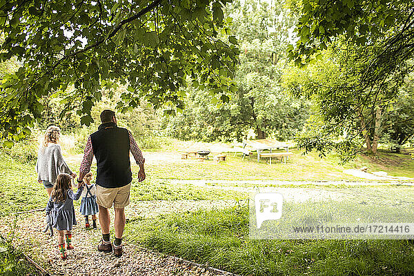 Familie  die sich an den Händen hält  geht auf einem Pfad in einem idyllischen Park spazieren