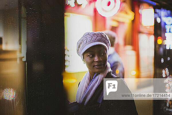 Junge Frau mit Hut schaut über die Schulter an der Bushaltestelle in der Nacht