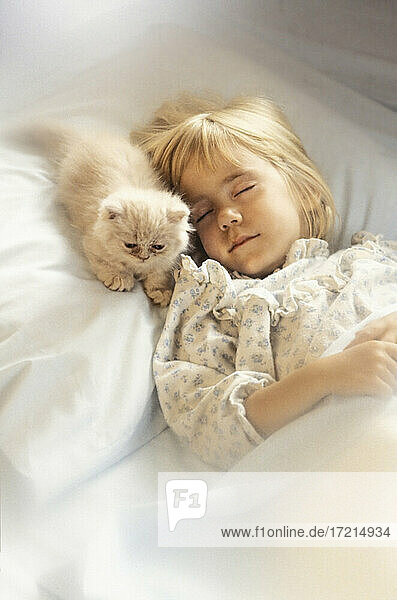 Mädchen (6-7) mit Kätzchen schlafend im Bett