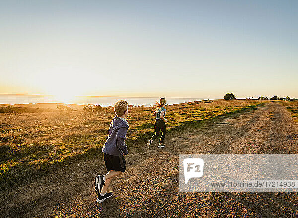 Vereinigte Staaten  Kalifornien  Cambria  Rückansicht eines Jungen (10-11) und eines Mädchens (12-13)  die auf einem Fußweg in einer Landschaft bei Sonnenuntergang laufen