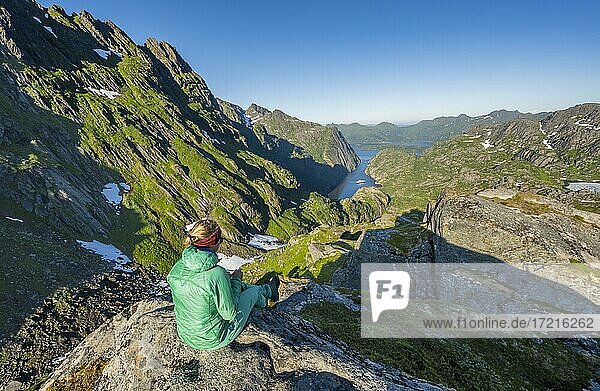 Wanderin  junge Frau sitzt auf Felsen  Boot im Fjord Trollfjord  Berge und Raftsund  Lofoten  Nordland  Norwegen  Europa
