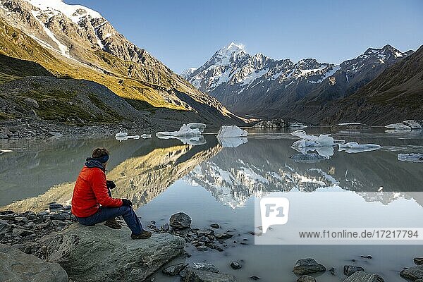 Hiker  young man sitting on a rock  Mount Cook in morning light  Hooker Lake with reflection  sunrise  Mount Cook National Park  Southern Alps  Hooker Valley  Canterbury  South Island  New Zealand  Oceania