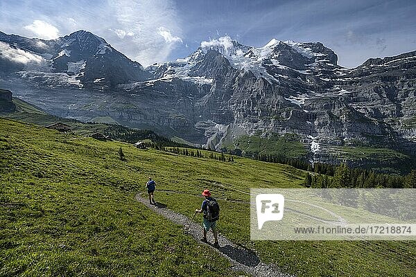 Two hikers on a hiking trail  in front of the Eiger north face  behind mountains and mountain tops  steep face and mountains  Jungfrau region  Lauterbrunnen  Bernese Alps  Switzerland  Europe