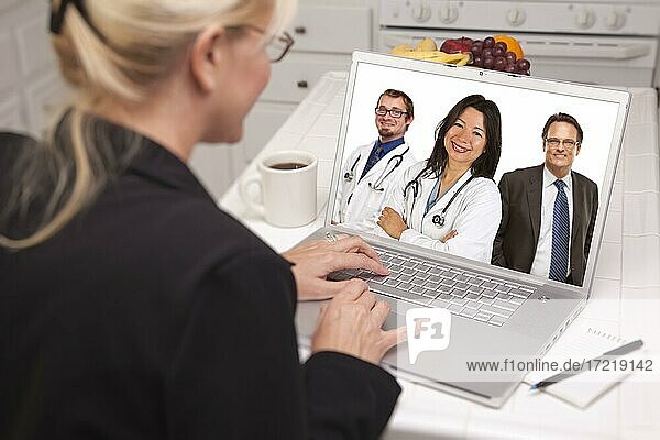 Over shoulder of woman in kitchen using laptop online chat with nurses or doctors on screen