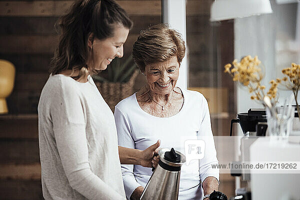 Lächelnde junge Frau  die zu Hause bei ihrer Großmutter einen Wasserkocher hält