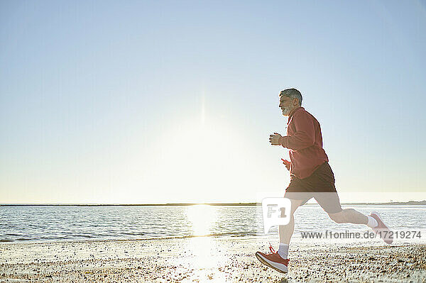 Männlicher Läufer  der bei Sonnenuntergang am Strand joggt