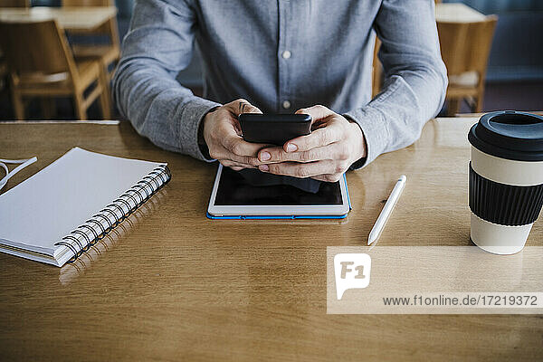 Businessman using smart phone over digital tablet on desk at work place
