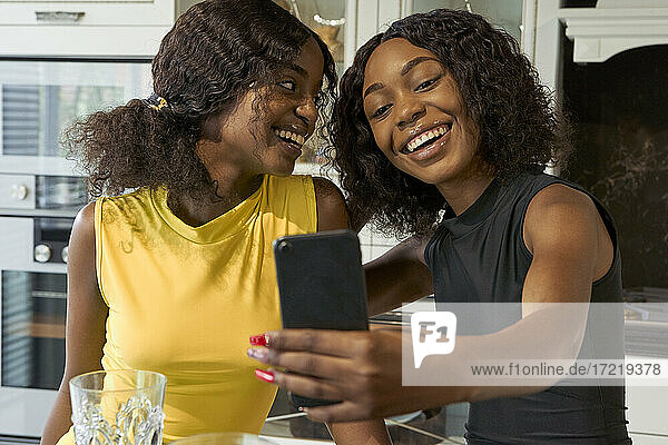 Portrait of two happy friends taking selfie with smartphone in the kitchen