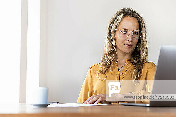 Geschäftsfrau mit Brille  die im Heimbüro auf einen Laptop schaut