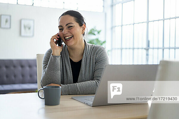 Geschäftsfrau lacht  während sie zu Hause mit dem Handy telefoniert