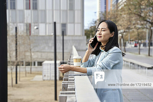 Businesswoman looking away while talking on mobile phone at footpath