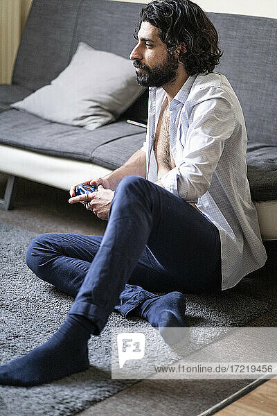 Junger Mann spielt ein Videospiel  während er zu Hause vor dem Sofa sitzt