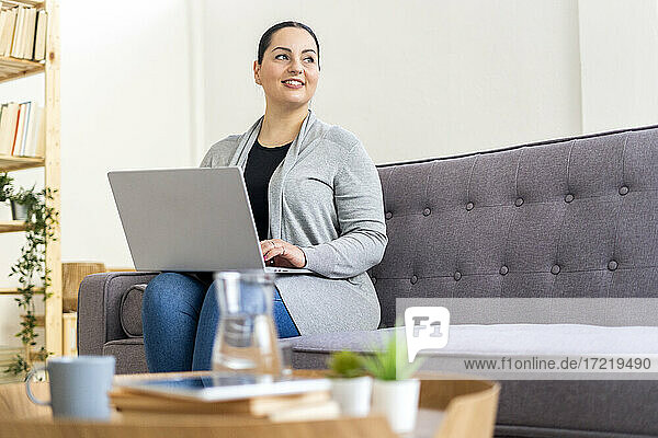 Frau  die wegschaut  während sie mit ihrem Laptop auf dem Sofa zu Hause sitzt