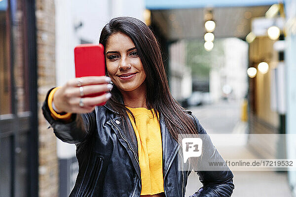 Lächelnde Frau nimmt Selfie durch Handy in der Stadt