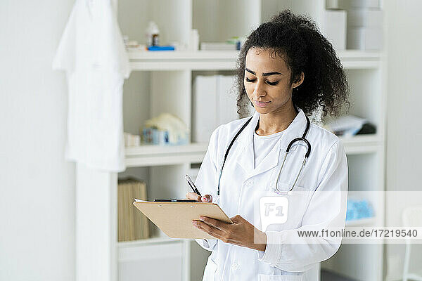 Junge Ärztin schreibt auf einem Klemmbrett  während sie in einer Klinik arbeitet