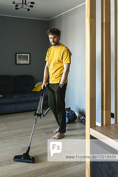 Mid adult man using vacuum cleaner while cleaning floor at home