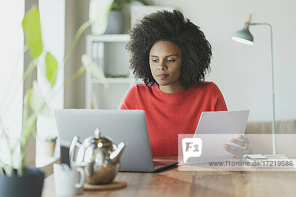 Curly hair woman with paper working on laptop at home