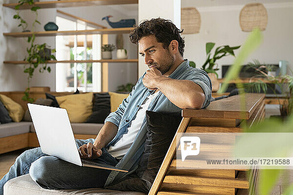 Concentrated freelance worker using laptop while sitting on couch at home