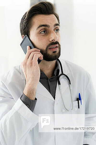 Handsome male healthcare worker talking on smart phone while looking away