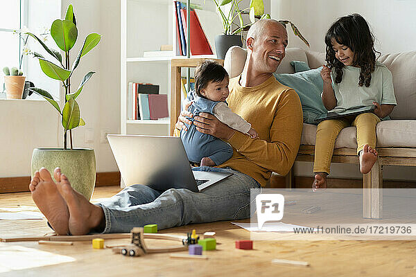 Lächelnder Vater mit Laptop  der mit seinen Töchtern zu Hause spielt