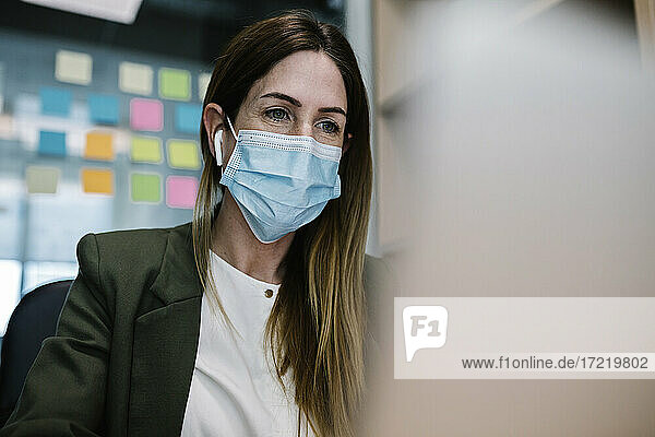 Unternehmerin mit Gesichtsschutzmaske bei der Arbeit im Büro während COVID-19
