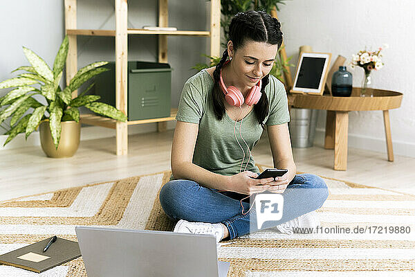 Frau mit Kopfhörern  die ein Smartphone benutzt  während sie zu Hause sitzt