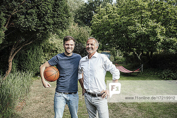 Smiling son with basketball standing with father in backyard