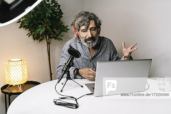 Männlicher leitender Angestellter gestikuliert  während er im Büro zu Hause über seinen Laptop podcastet