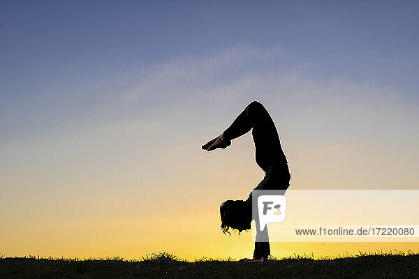 Flexible young woman in silhouette doing handstand