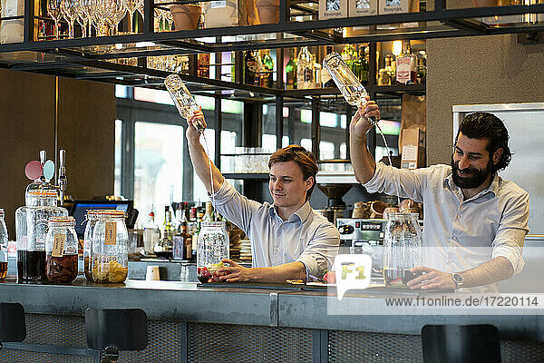 Ein lächelnder Barkeeper und ein Auszubildender gießen Alkohol in ein Glas am Bartresen