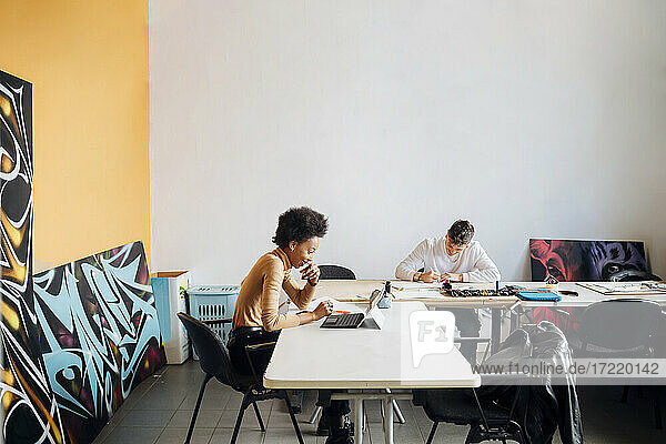 Lächelnde junge Frau  die einen Laptop benutzt  während ein Mann am Tisch sitzend in einem Studio übt