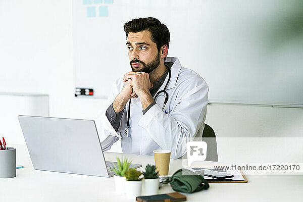 Male healthcare worker sitting with hand on chin while looking away