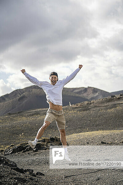 Aufgeregter männlicher Tourist mit ausgestreckten Armen beim Sprung auf den Vulkan el cuervo