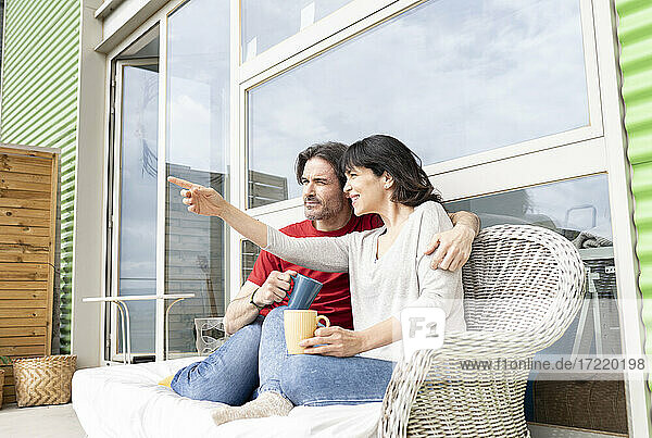 Frau  die auf einen Mann zeigt  während sie auf einem Sofa auf dem Balkon sitzt