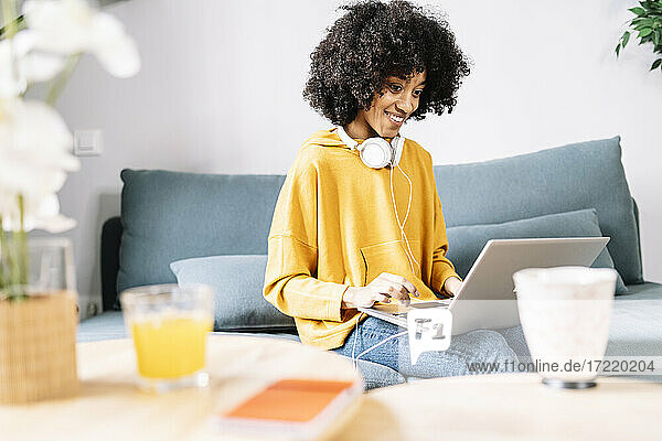 Frau mit Kopfhörern  die einen Laptop benutzt  während sie zu Hause auf dem Sofa sitzt