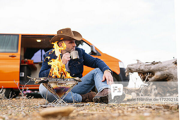 Reifer Mann  der vor einem Campingkocher sitzt und Kaffee trinkt