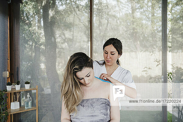 Female physiotherapist applying elastic therapeutic tape to patient's shoulder in hospital