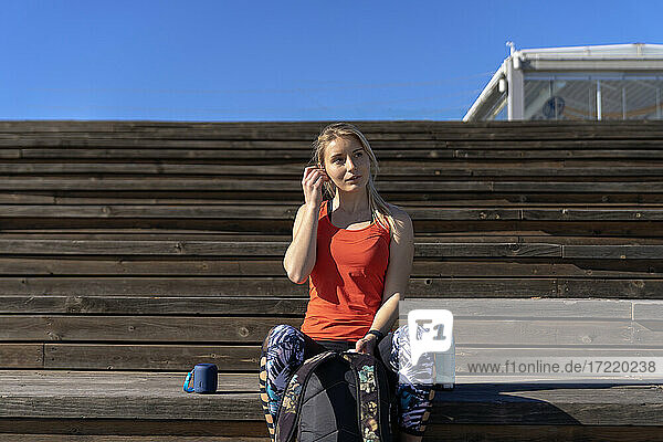 Nachdenkliche Sportlerin auf dem Pier sitzend an einem sonnigen Tag