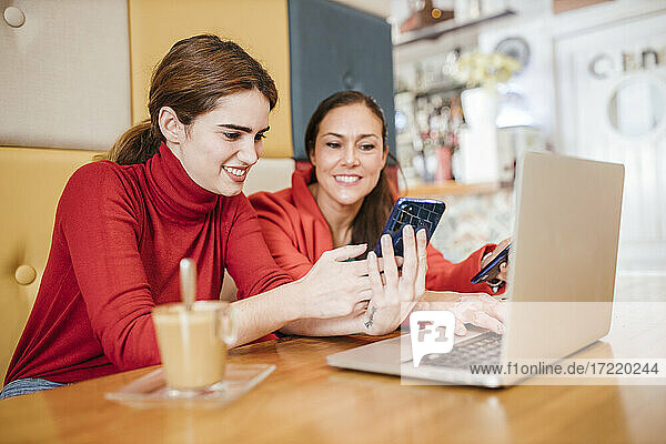 Lächelnde Unternehmerin  die ein Mobiltelefon benutzt  während sie neben einem Kollegen in einem Café sitzt