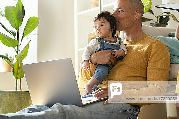 Vater mit Laptop  der sein Baby küsst  während er zu Hause sitzt