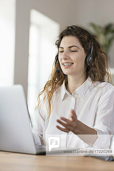 Contented female customer service representative with headphones explaining to client headphones at desk in home office