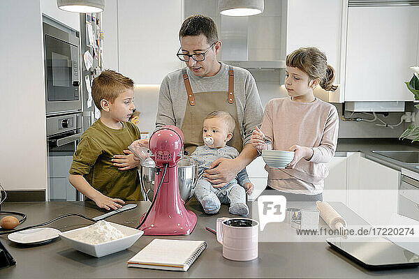 Mid adult man with baby boy preparing food with children at home