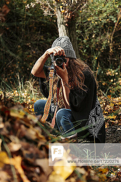 Mid adult woman photographing with camera in forest during autumn