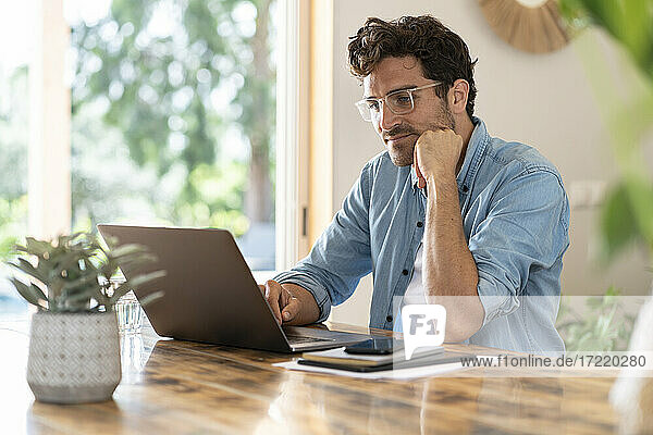 Serious male freelancer with head in hands working on laptop at home office