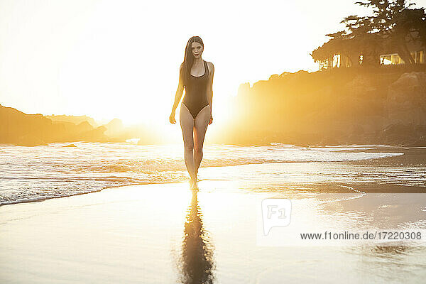 Fashion model in black one piece swimsuit walking in water during sunset