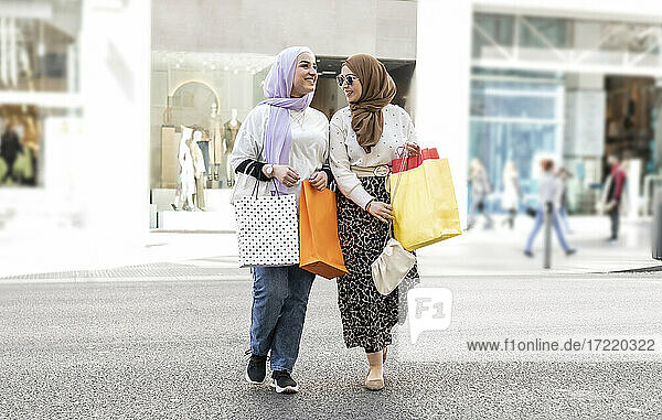 Female Arab friends crossing road while shopping in city