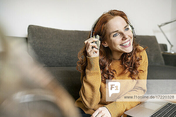 Lächelnde schöne Frau mit Kopfhörern  während sie zu Hause am Laptop auf dem Couchtisch sitzt