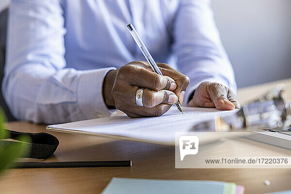 Männlicher Unternehmer beim Unterschreiben eines Dokuments am Schreibtisch im Büro