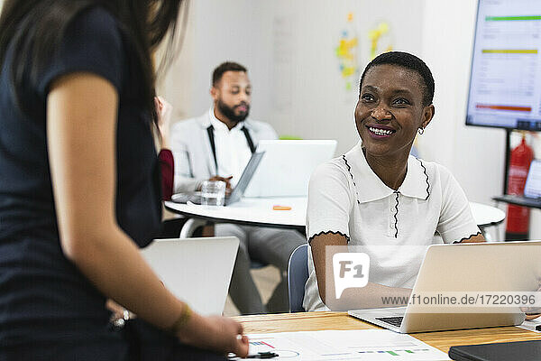 Lächelnde Geschäftsfrau schaut einen Kollegen im Büro an