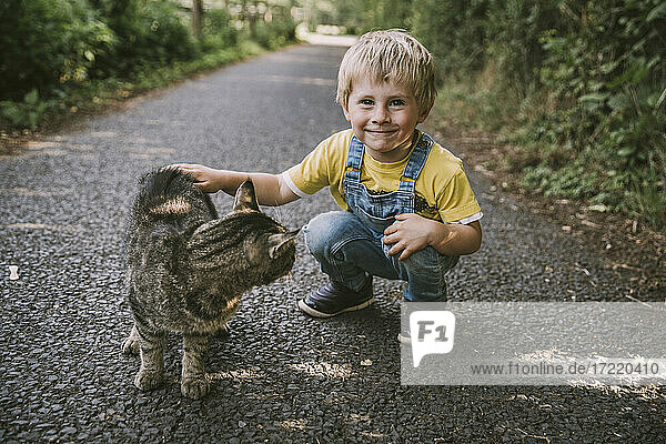 Lächelnder Junge hockt und streichelt eine streunende Katze auf der Straße